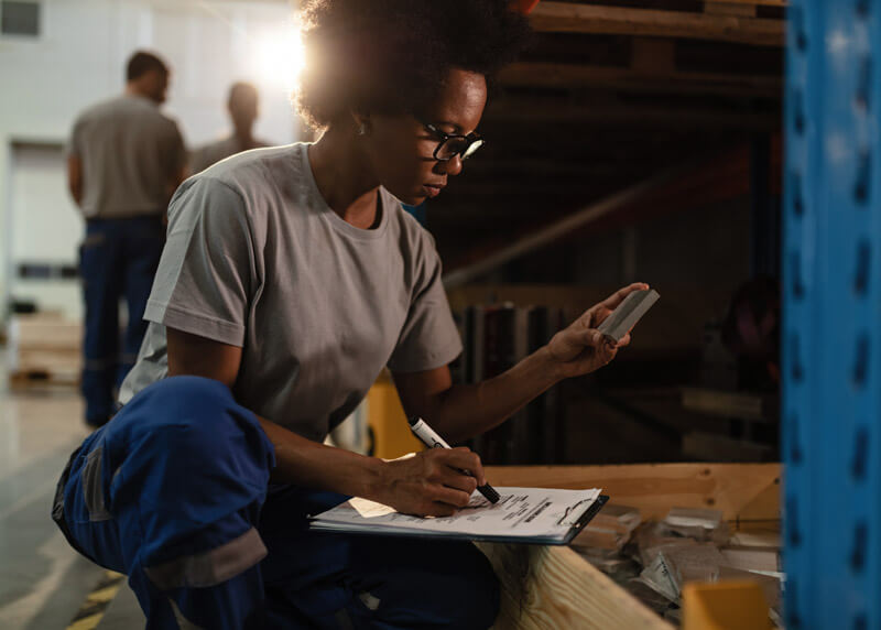 Black American female worker checking products before the shipment and taking notes in a warehouse.
