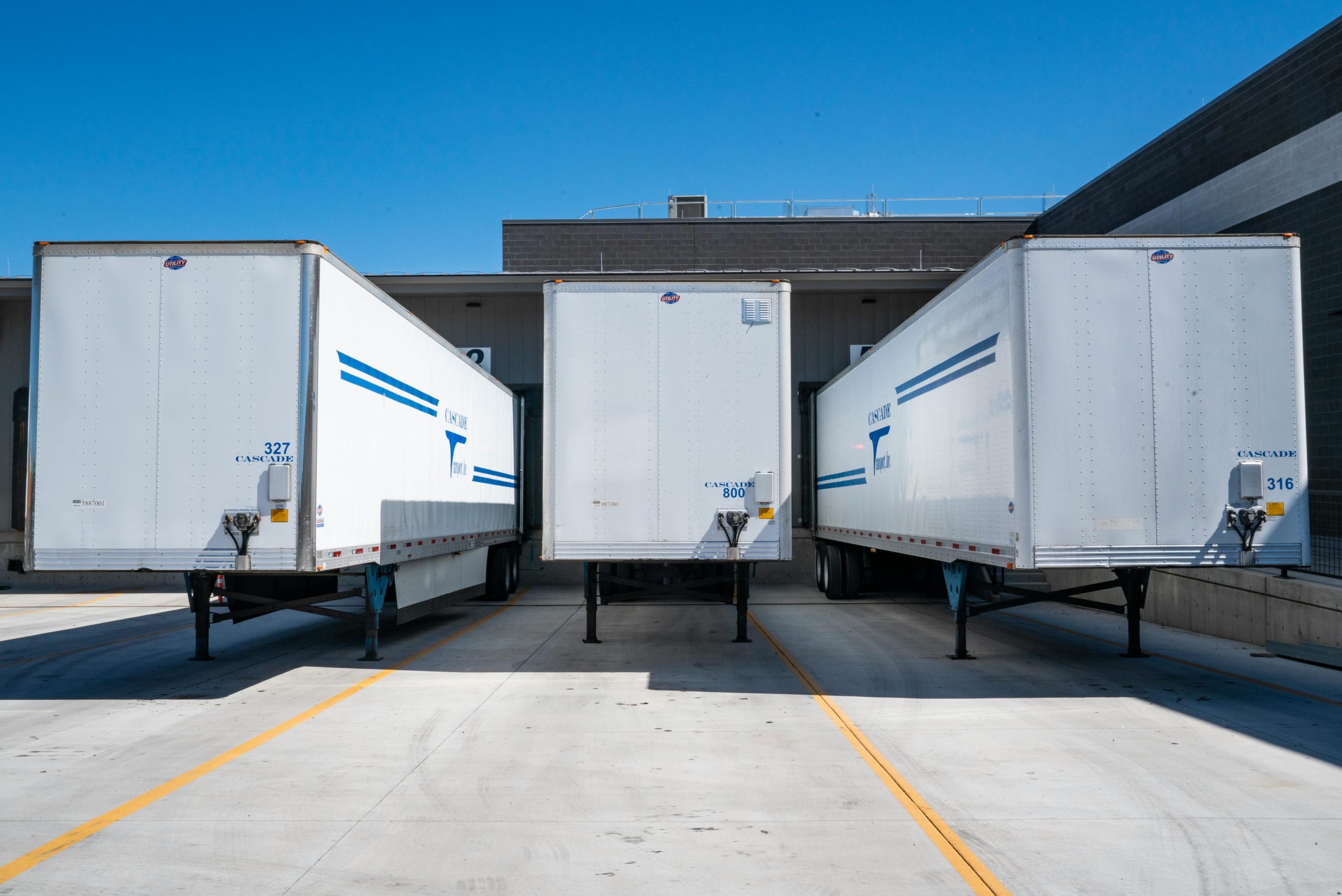 3 white truck trailers in a row at a dock.