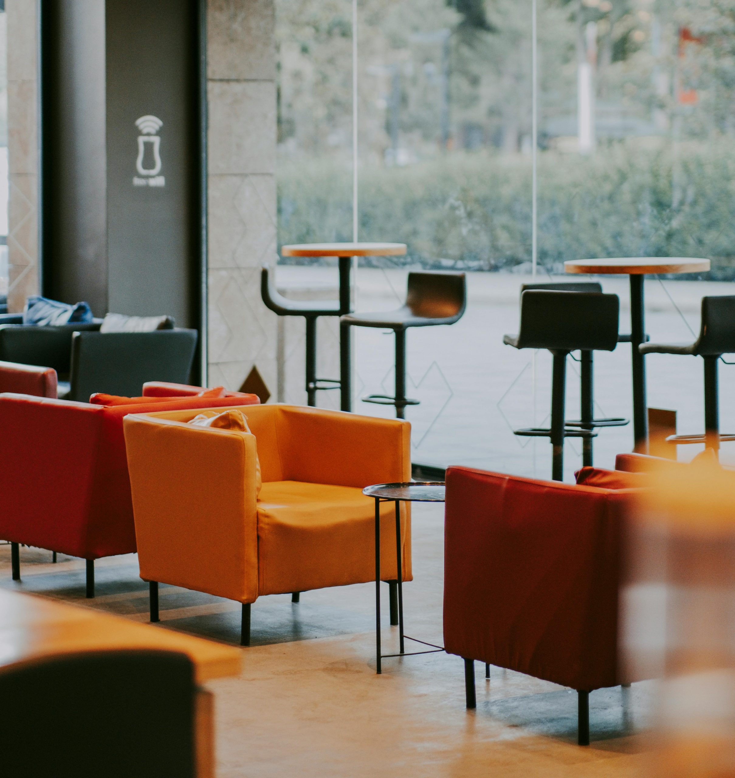 Cafe interior with an assortment of orange and red upholstered chairs with tables and stools in the background.