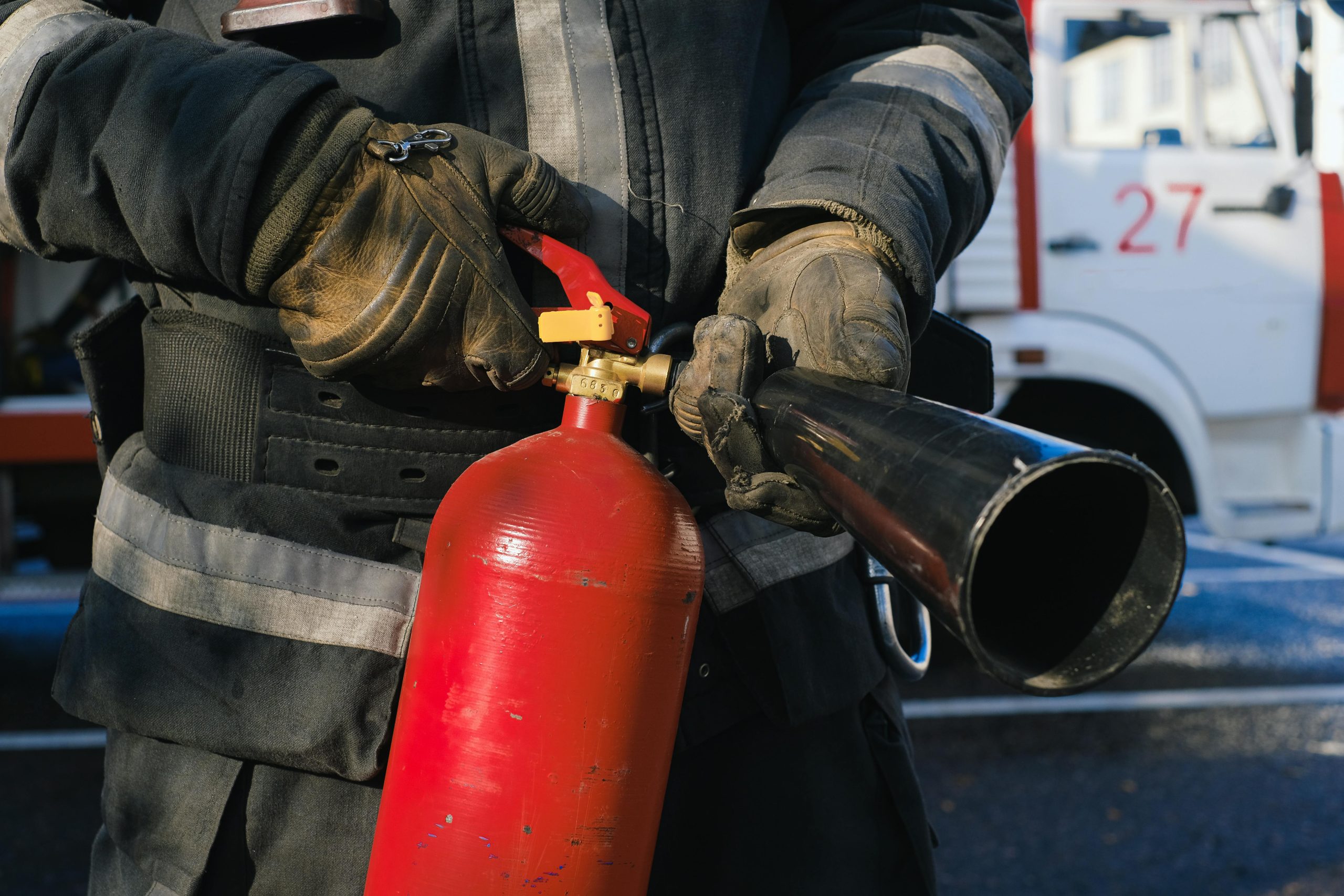 Close up of a firefighter holding a red fire extinguisher.