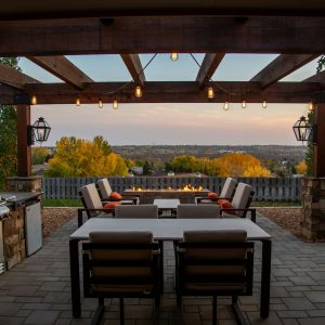 Back patio with an outdoor kitchen, grill, pergola, hanging lights, and 2 sets of outdoor dining tables with chairs.