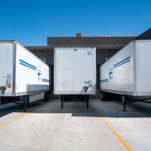 3 white truck trailers in a row at a dock.