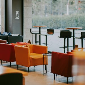 Cafe interior with an assortment of orange and red upholstered chairs with tables and stools in the background.