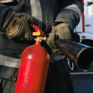 Close up of a firefighter holding a red fire extinguisher.